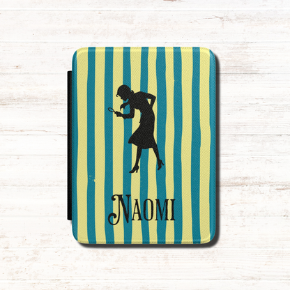 A close-up of a Personalised Nancy Drew Kindle Case, featuring a blue and yellow vertical stripe pattern with a black silhouette of Nancy Drew holding a magnifying glass and a custom name in vintage style typography at the bottom. Designed by Starlit Prose Bookish Merch Australia.