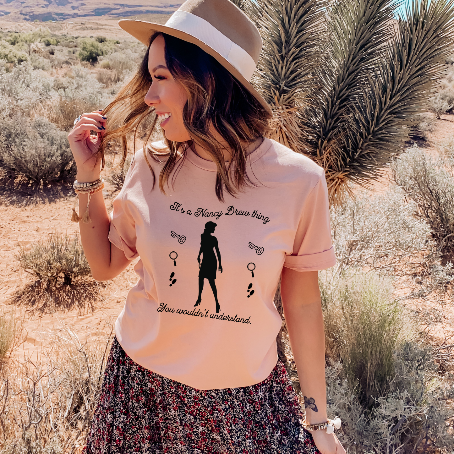 heather peach tshirt with text that says "It's a Nancy Drew thing, you wouldn't understand" with graphic elements like a key, magnifying glass and footsteps.
