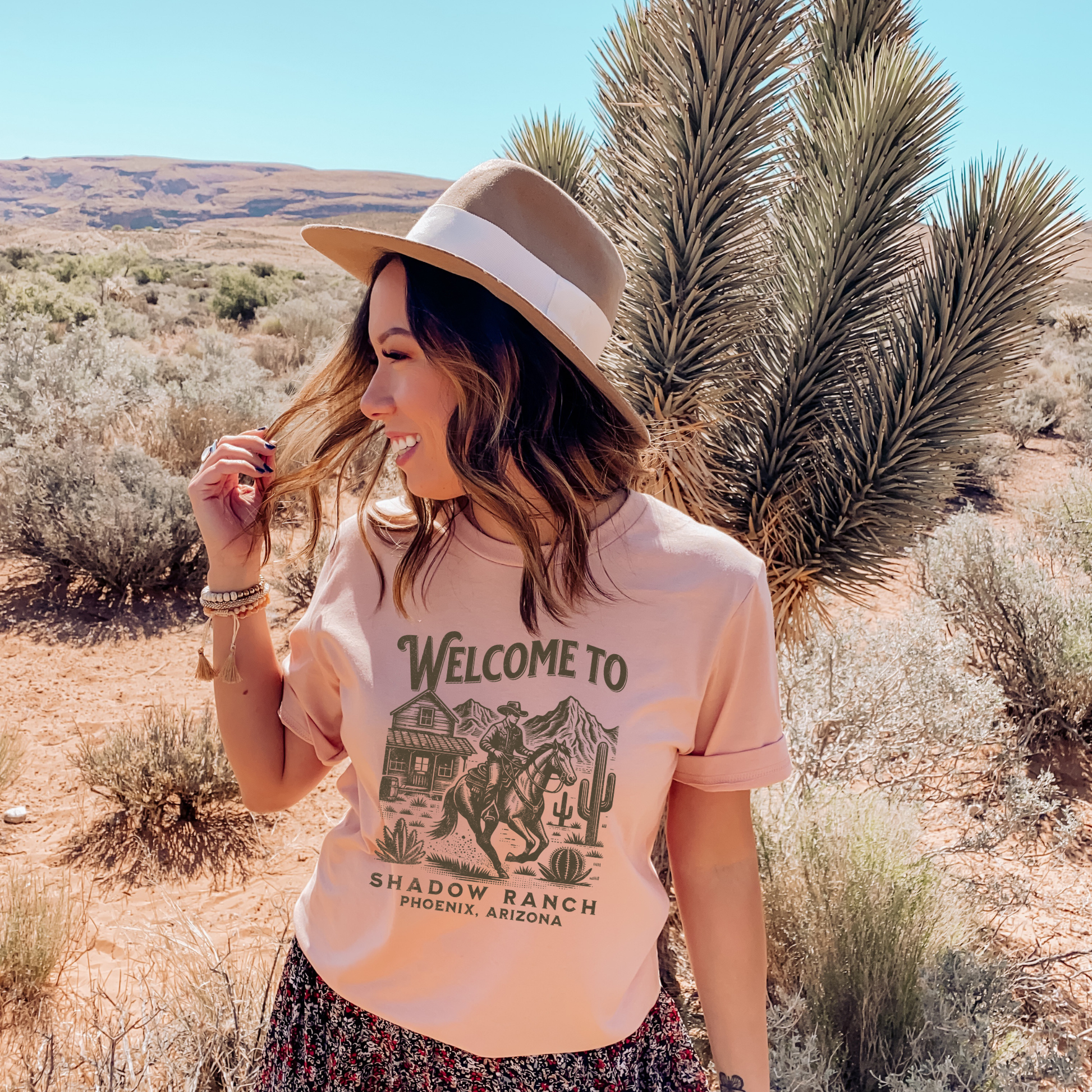heather peach shirt that says "Welcome to Shadow Ranch Phoenix, Arizona" with a retro graphic of a cowboy riding on a horse.