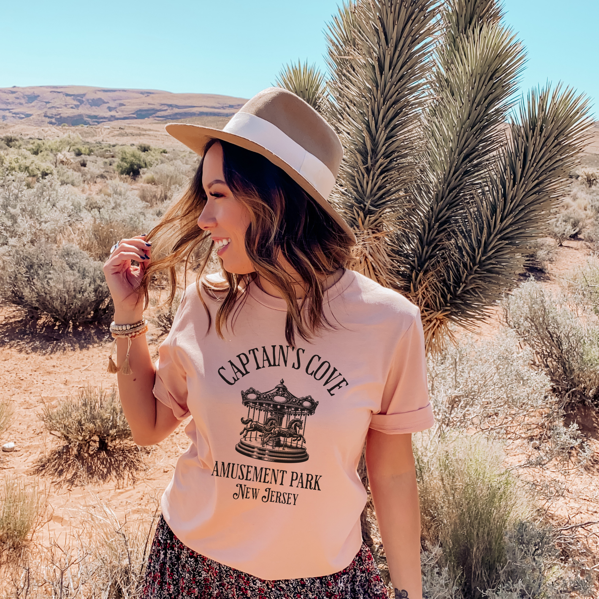 Woman wearing a 'Captain's Cove Amusement Park New Jersey' t-shirt Heather Peach colour in a desert setting.