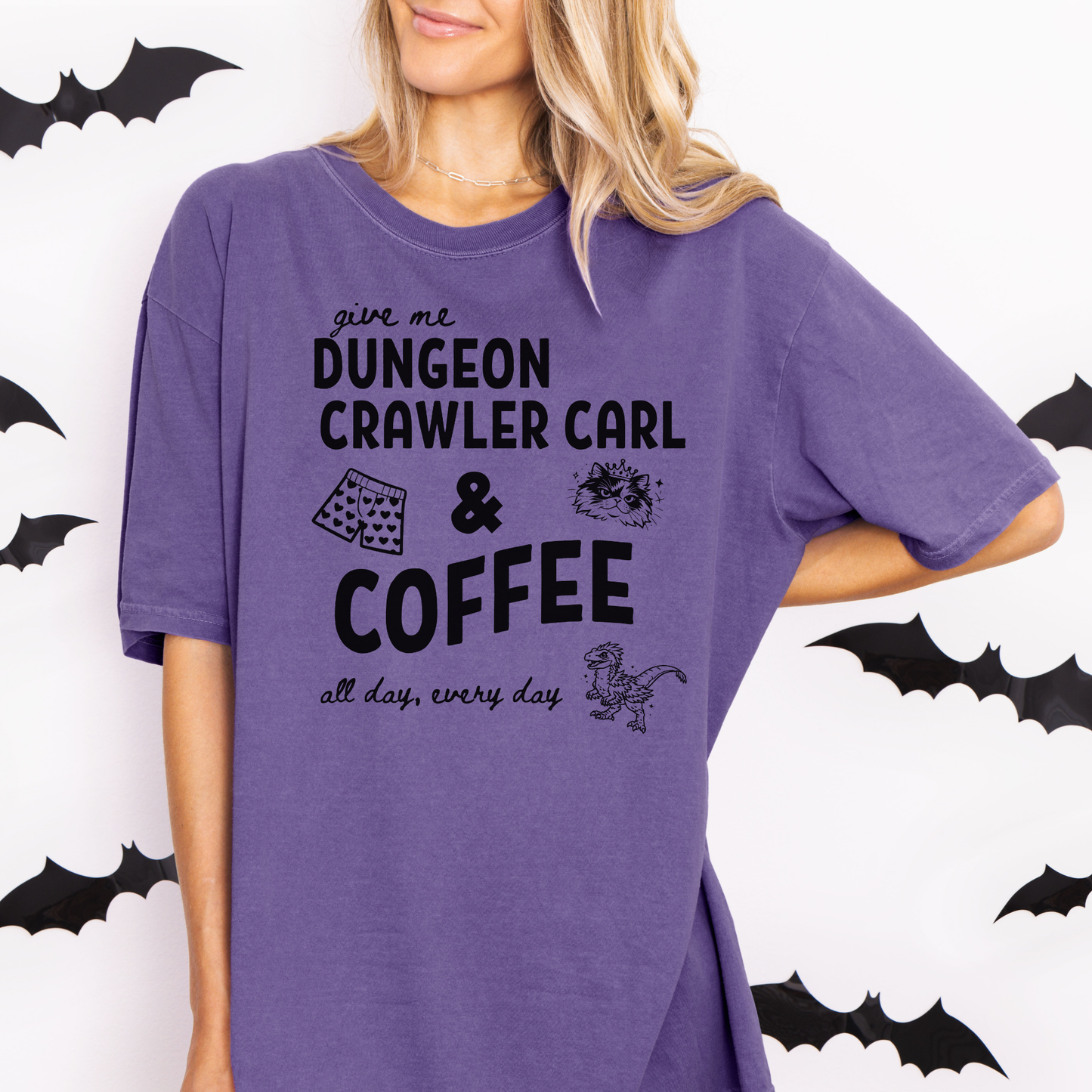 A woman wearing an oversized Grape graphic Comfort colors T-shirt with black text reading 'give me DUNGEON CRAWLER CARL & COFFEE all day, every day' and small illustrations - including Carl's pajama shorts, Princess Donut & Mongo. Designed by Starlit Prose, Bookish Merch Australia