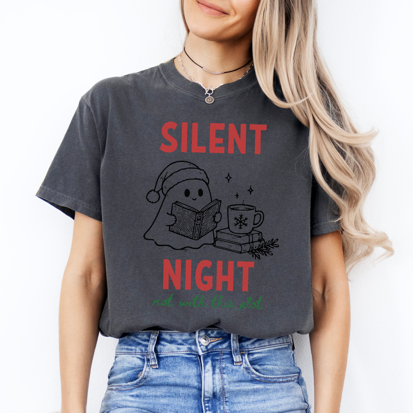 A woman wearing a Pepper Comfort Colors t-shirt with a cute doodle illustration of a ghost reading a book, with a cup of coffee stacked on some books. There's bold text that says  'SILENT NIGHT" in red, with green cursive that says " not with this plot". Designed by Starlit Prose Bookish Merch Australia.