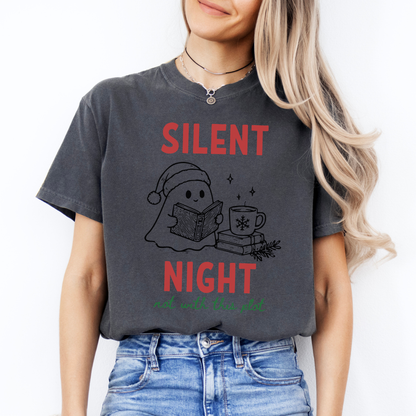 A woman wearing a Pepper Comfort Colors t-shirt with a cute doodle illustration of a ghost reading a book, with a cup of coffee stacked on some books. There's bold text that says  'SILENT NIGHT" in red, with green cursive that says " not with this plot". Designed by Starlit Prose Bookish Merch Australia.