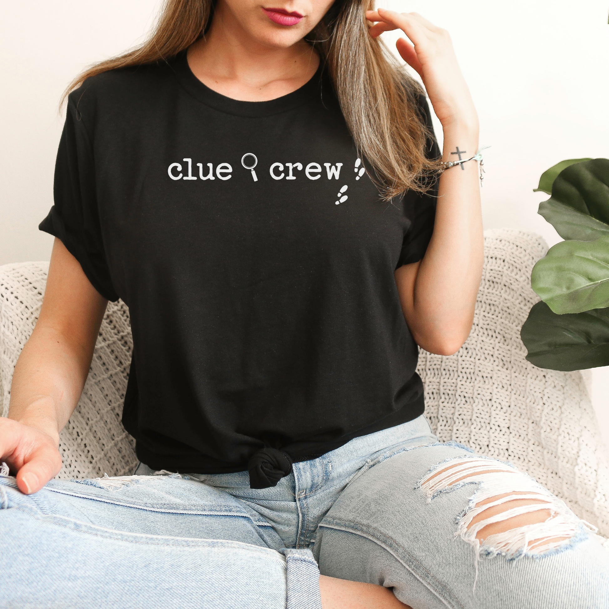 Person wearing a black t-shirt with 'clue crew' text, sitting on a couch.