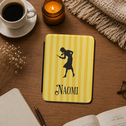 A close-up of a Personalised Nancy Drew Kindle Case, featuring a yellow vertical stripe pattern with a black silhouette of Nancy Drew holding a magnifying glass and a custom name in vintage style typography at the bottom. Designed by Starlit Prose Bookish Merch Australia.
