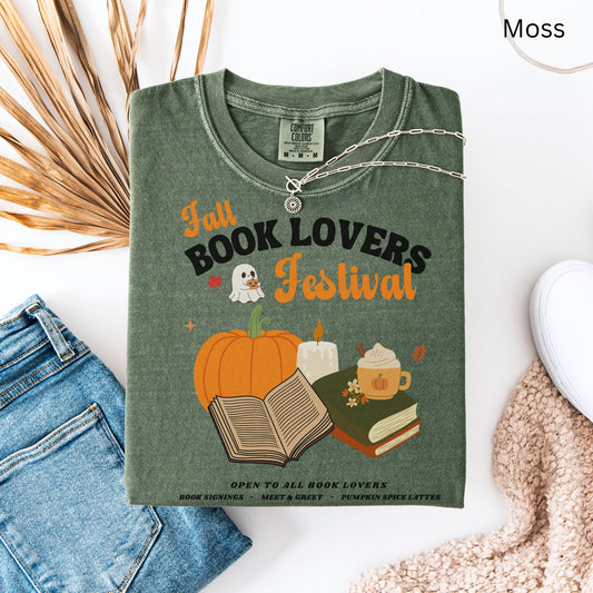 Woman wearing a Moss Green Comfort Colors Tshirt with 'Fall Book Lovers Festival' design featuring a pumpkin, books, and a ghost for a fictional Book Lovers Festival. Starlit Prose Bookish Merch Australia