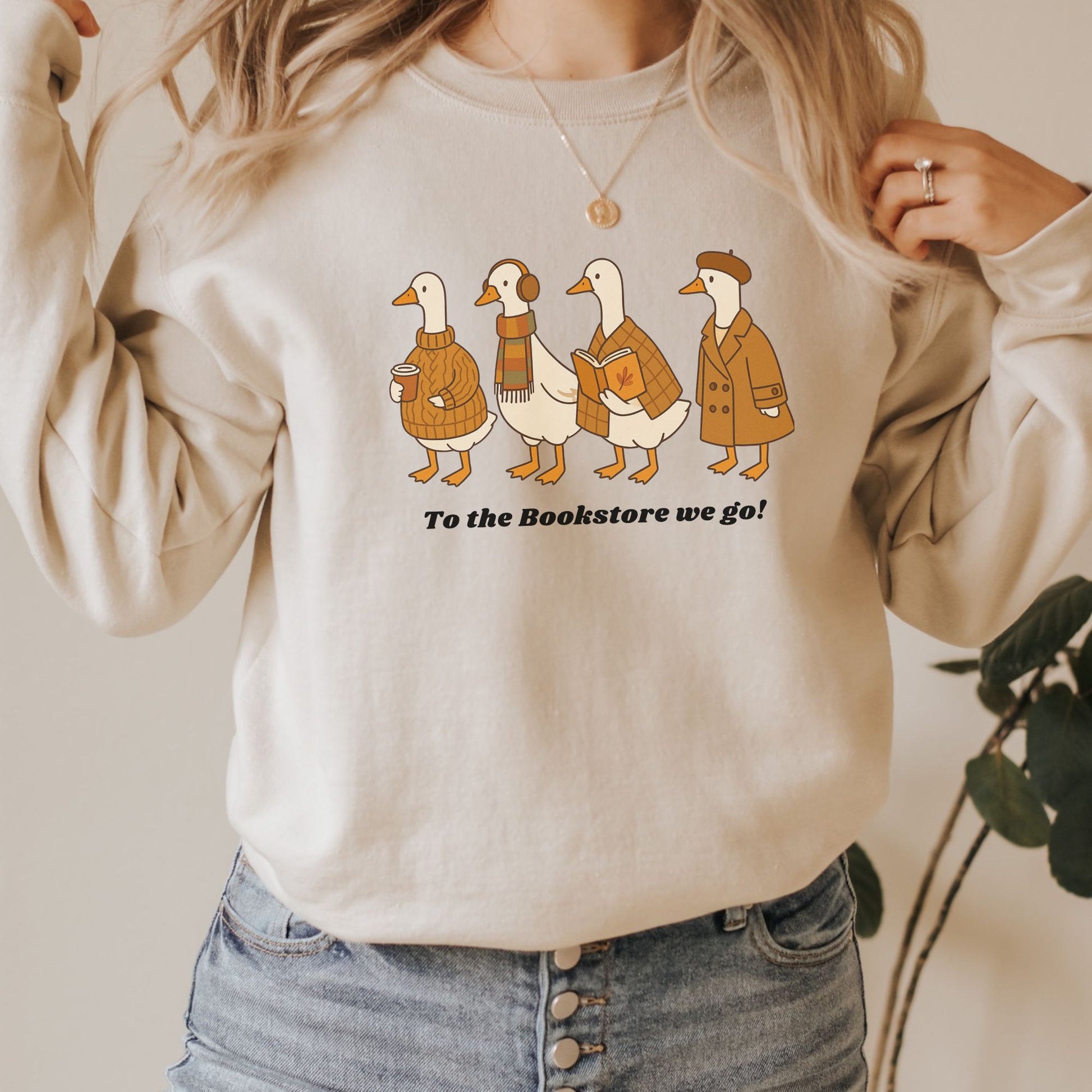 Sand sweatshirt with cartoon ducks and text 'To the Bookstore we go!' worn by a person. Starlit Prose Bookish Merch Australia