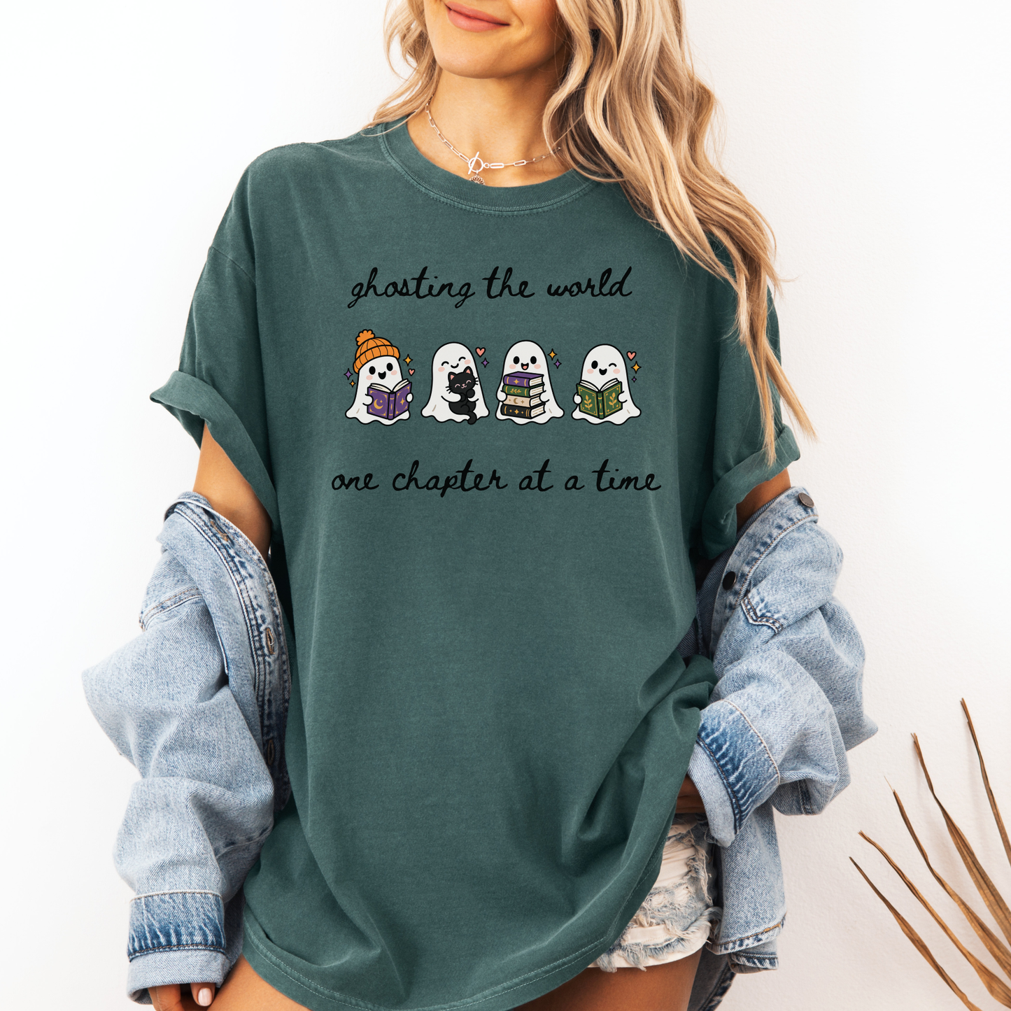 A woman wearing an oversized Seafoam Comfort Colors T-shirt with four cartoon ghosts reading books and the text 'ghosting the world one chapter at a time". Designed by Starlit Prose Bookish Merch Australia