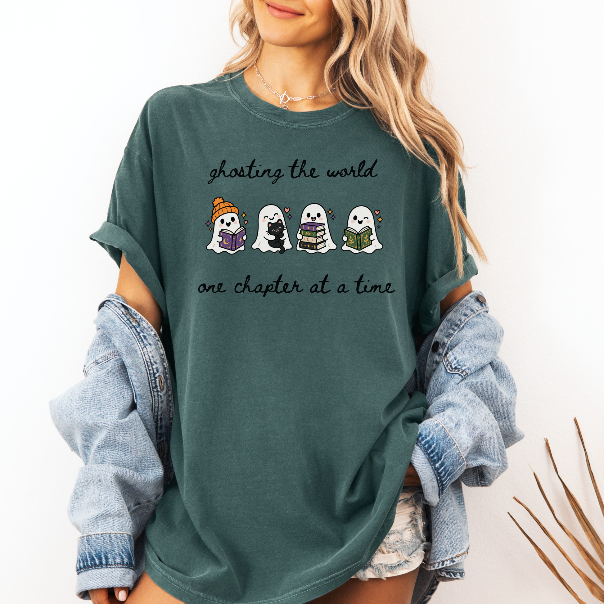 A woman wearing an oversized Seafoam Comfort Colors T-shirt with four cartoon ghosts reading books and the text 'ghosting the world one chapter at a time". Designed by Starlit Prose Bookish Merch Australia