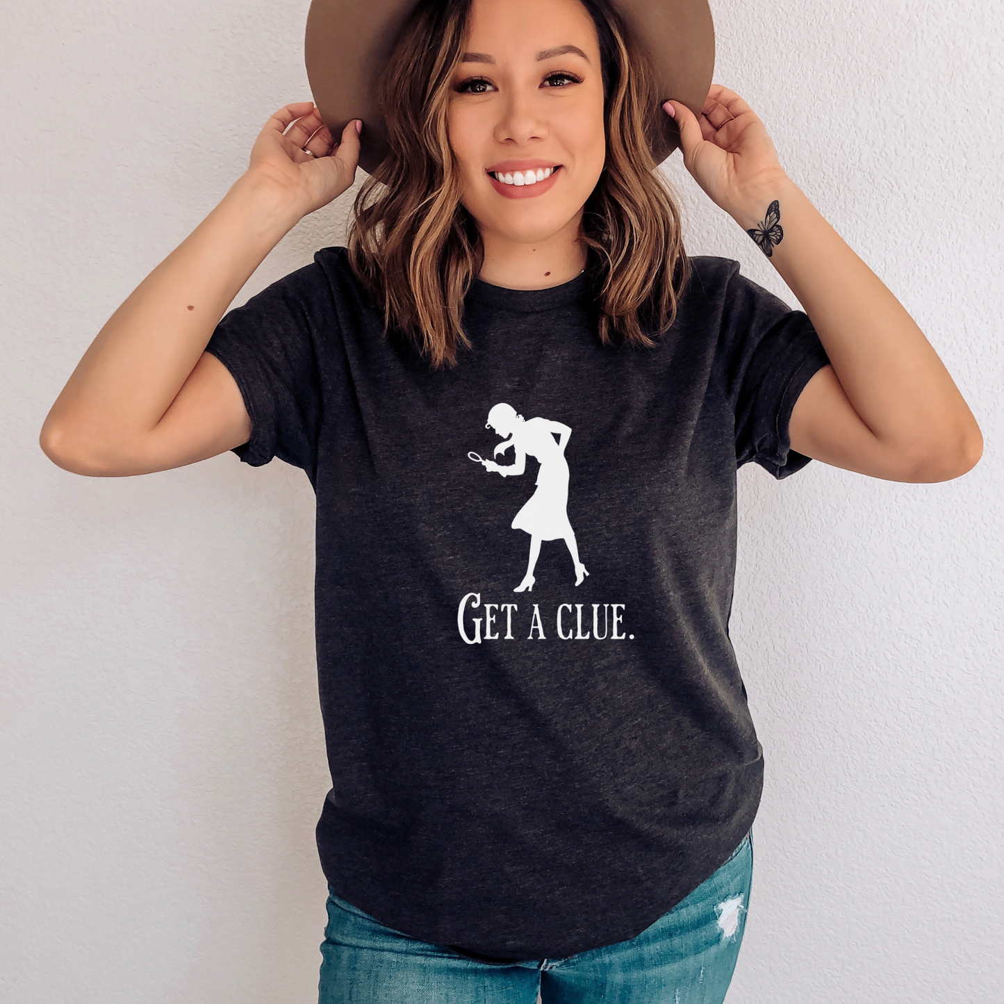 Woman wearing a dark grey heather t-shirt with a graphic and text, holding a hat.
