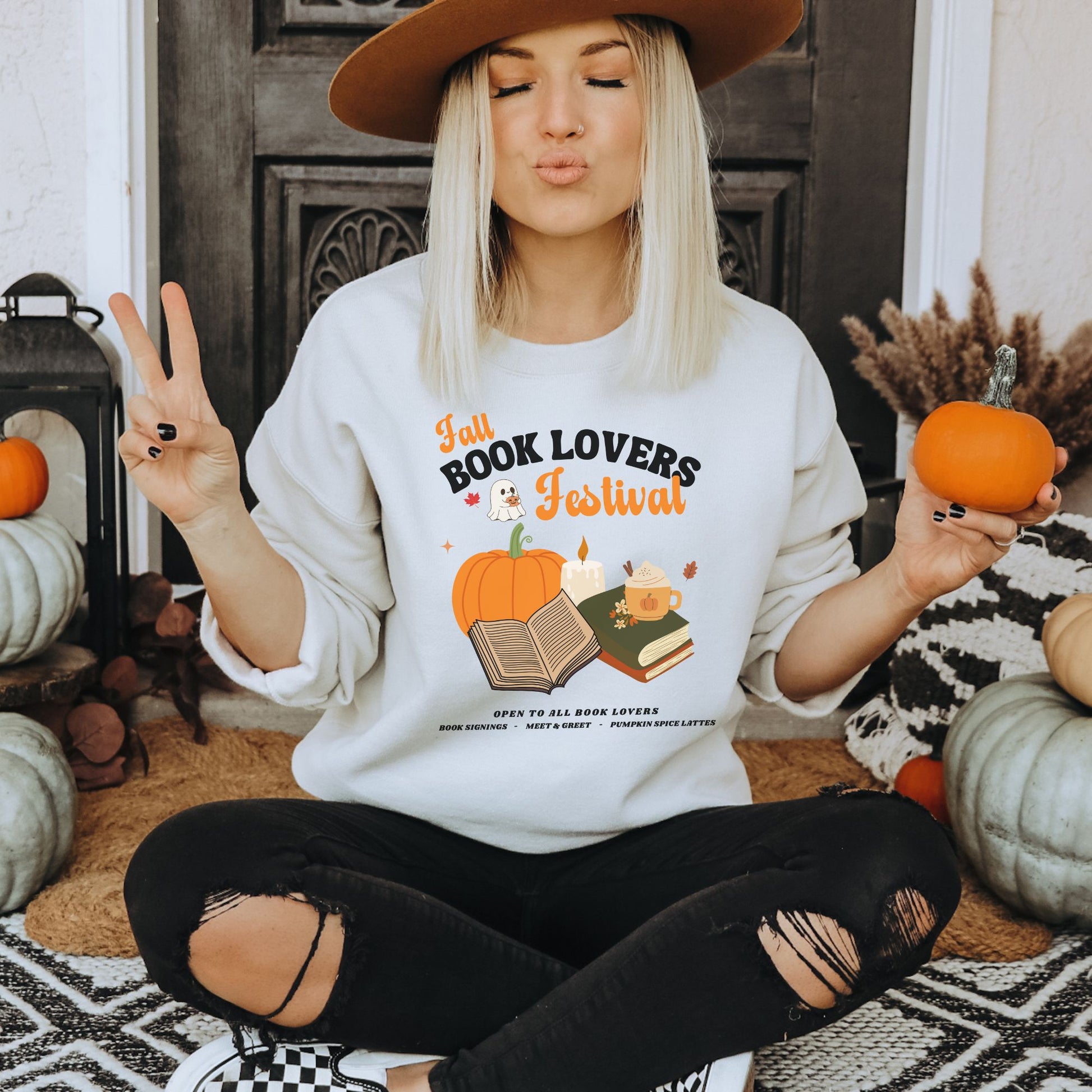 Woman wearing a White sweatshirt with 'Fall Book Lovers Festival' design featuring a pumpkin, books, and a ghost for a fictional Book Lovers Festival. Starlit Prose Bookish Merch Australia