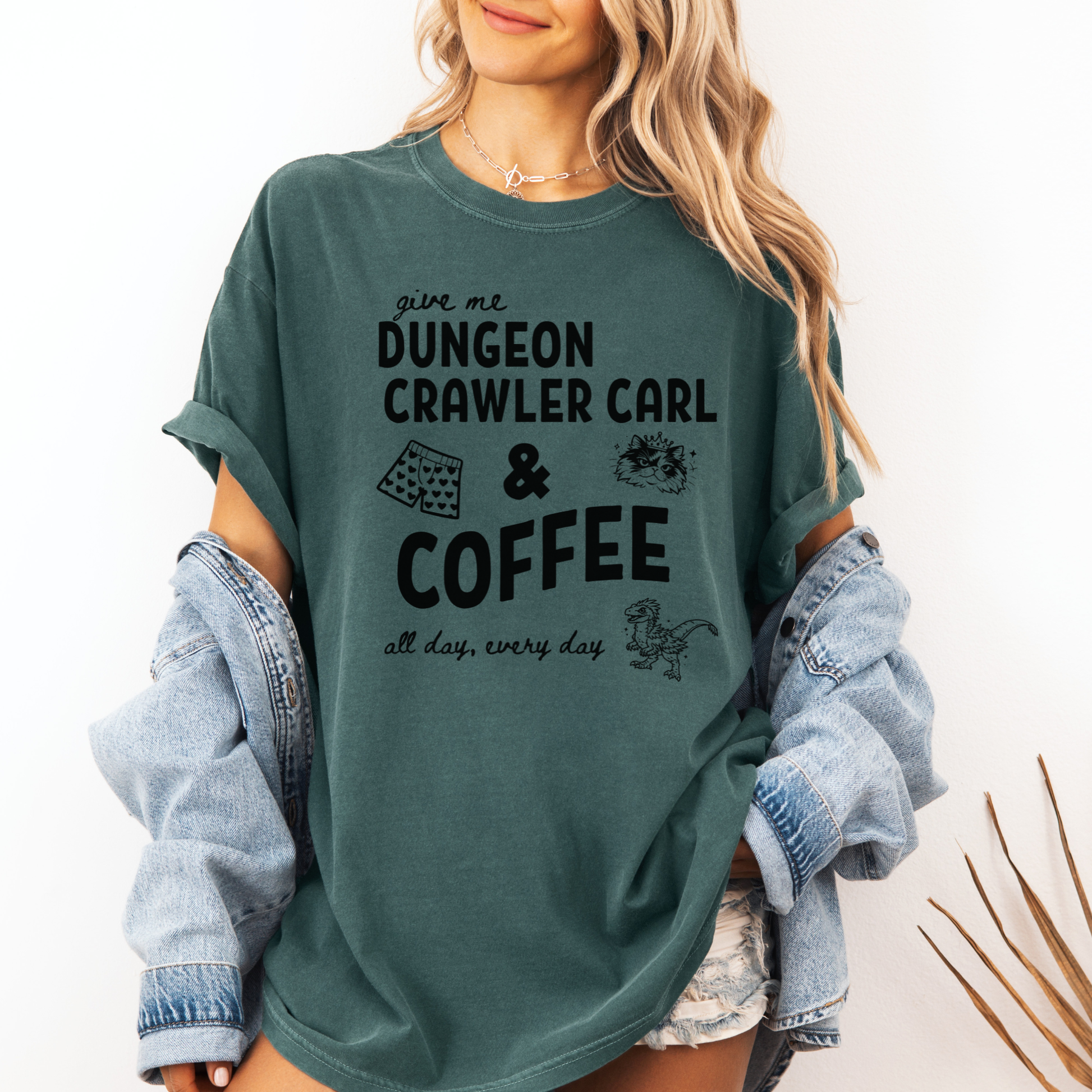 A woman wearing an oversized Seafoam Green graphic Comfort colors T-shirt with black text reading 'give me DUNGEON CRAWLER CARL & COFFEE all day, every day' and small illustrations - including Carl's pajama shorts, Princess Donut & Mongo. Designed by Starlit Prose, Bookish Merch Australia