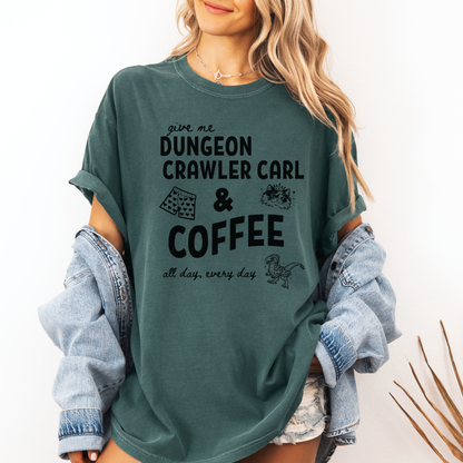 A woman wearing an oversized Seafoam Green graphic Comfort colors T-shirt with black text reading 'give me DUNGEON CRAWLER CARL & COFFEE all day, every day' and small illustrations - including Carl's pajama shorts, Princess Donut & Mongo. Designed by Starlit Prose, Bookish Merch Australia
