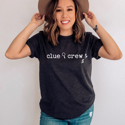 Woman wearing a Dark grey heather t-shirt with 'clue crew' text, holding a brown hat.