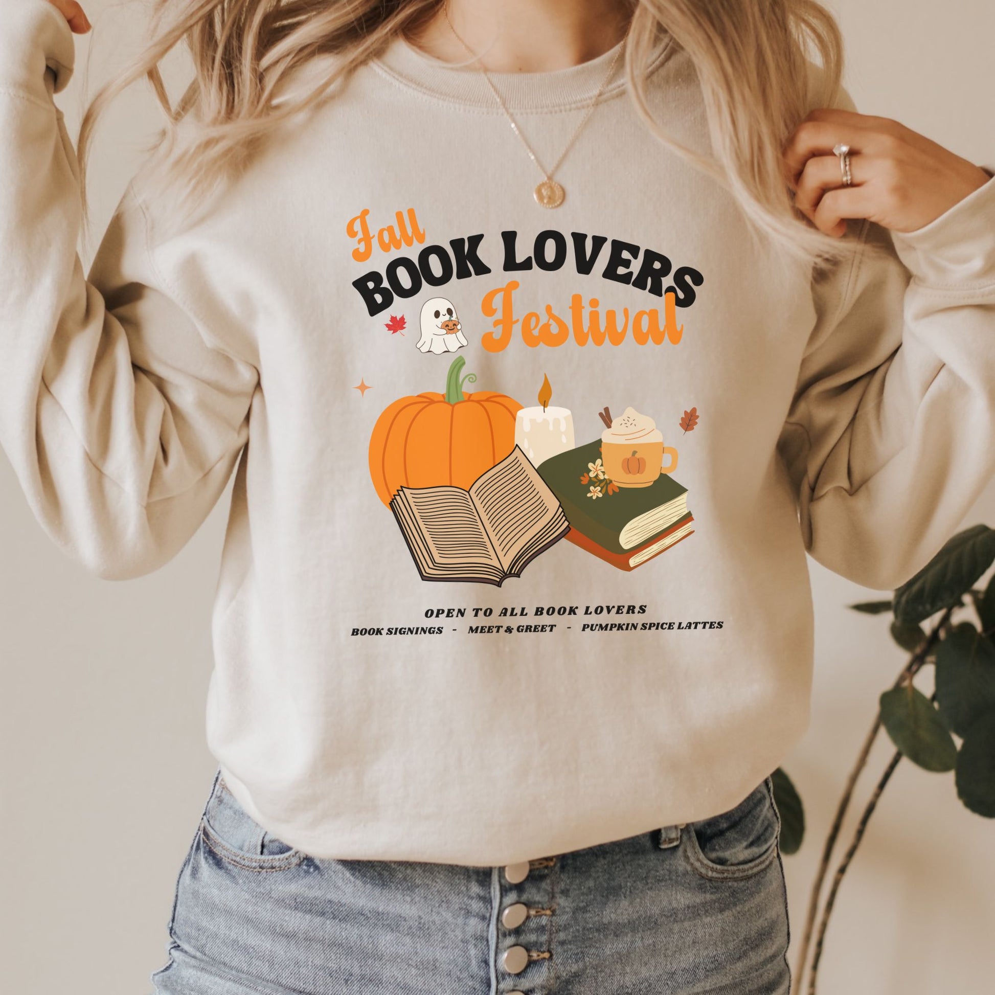 Woman wearing a Sand sweatshirt with 'Fall Book Lovers Festival' design featuring a pumpkin, books, and a ghost for a fictional Book Lovers Festival. Starlit Prose Bookish Merch Australia