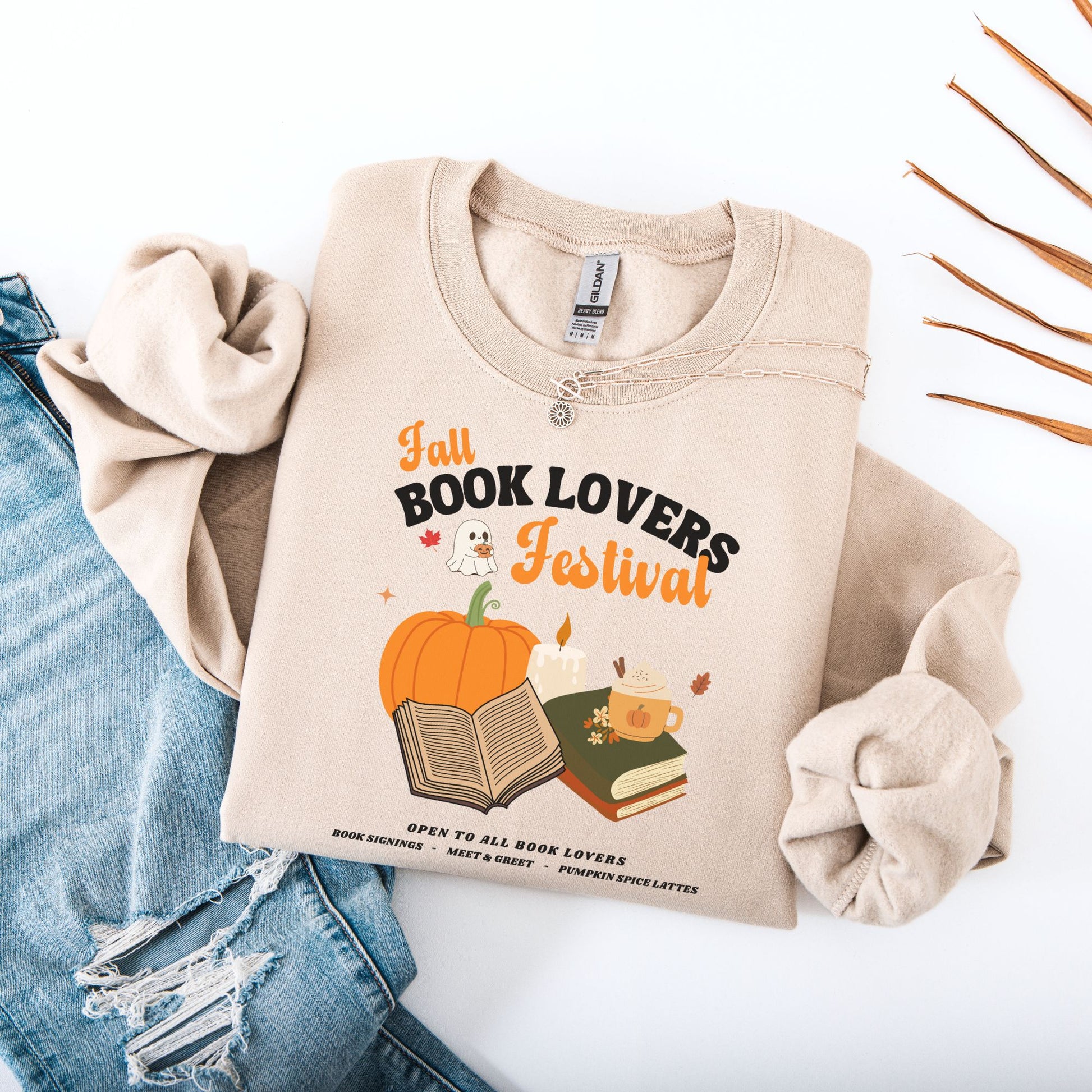 Flatlay of a Sand sweatshirt with 'Fall Book Lovers Festival' design featuring a pumpkin, books, and a ghost for a fictional Book Lovers Festival. Starlit Prose Bookish Merch Australia