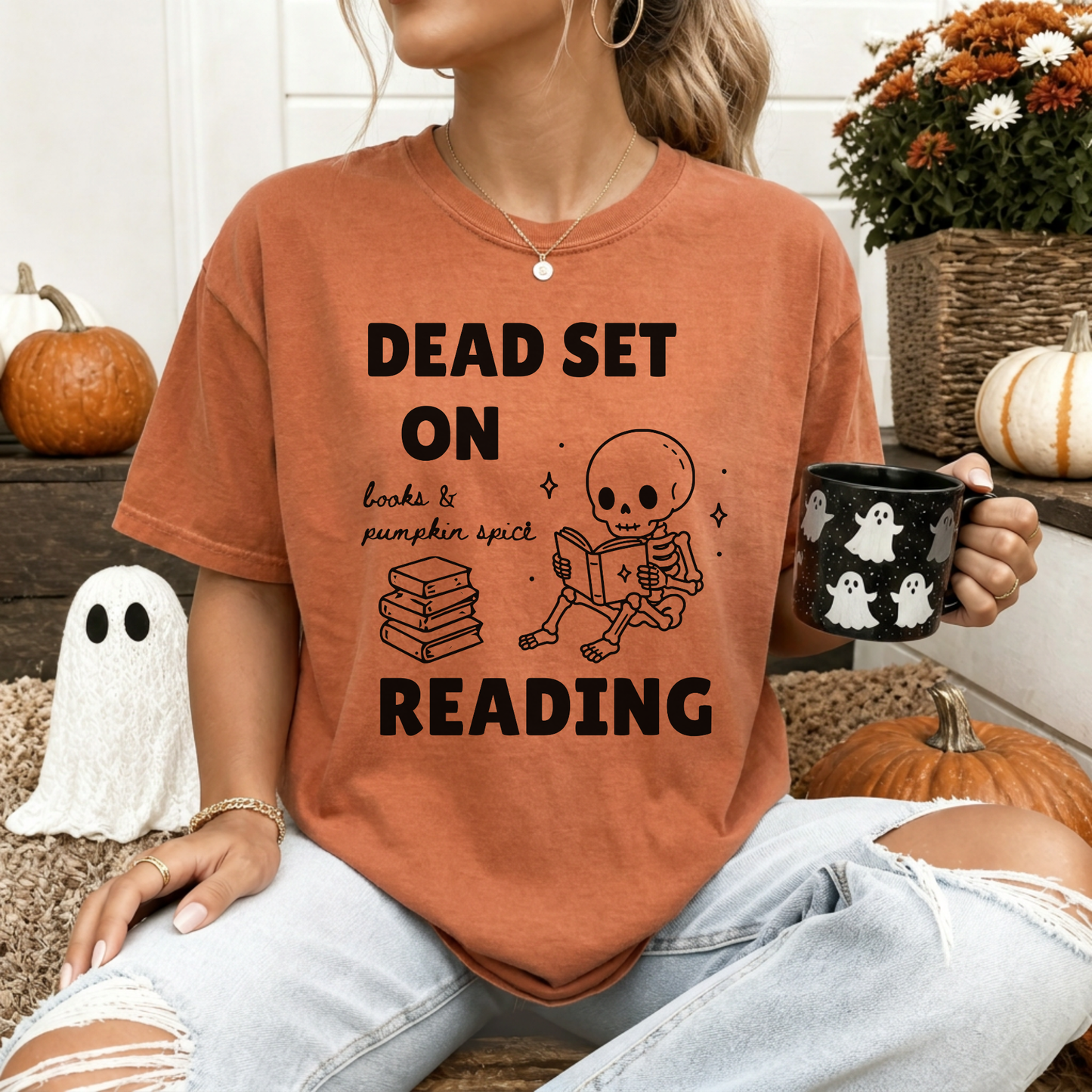A woman wearing a Yam orange Comfort Colors  t-shirt with a black print that reads 'DEAD SET ON READING' alongside a skeleton reading books and a stack of books. It also says books & pumpkin spice in script font. Designed by Starlit Prose Bookish Merch Australia