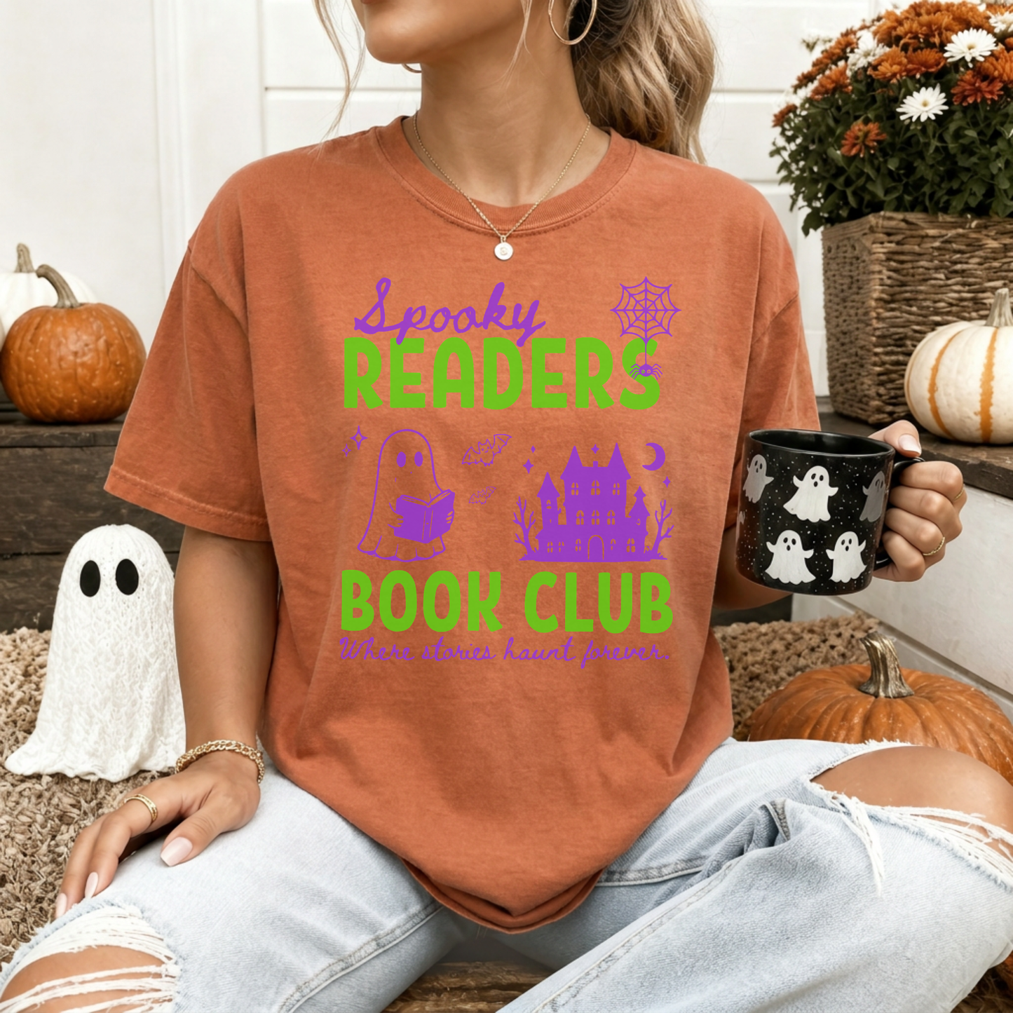  A woman wearing a Yam Orange Comfort colors graphic t-shirt with 'Spooky Readers Book Club' printed in green and purple, with Purple graphics including a cute ghost reading a book, a spider in its web & a haunted mansion paired with distressed blue jeans. Designed by Starlit Prose Bookish Merch Australia