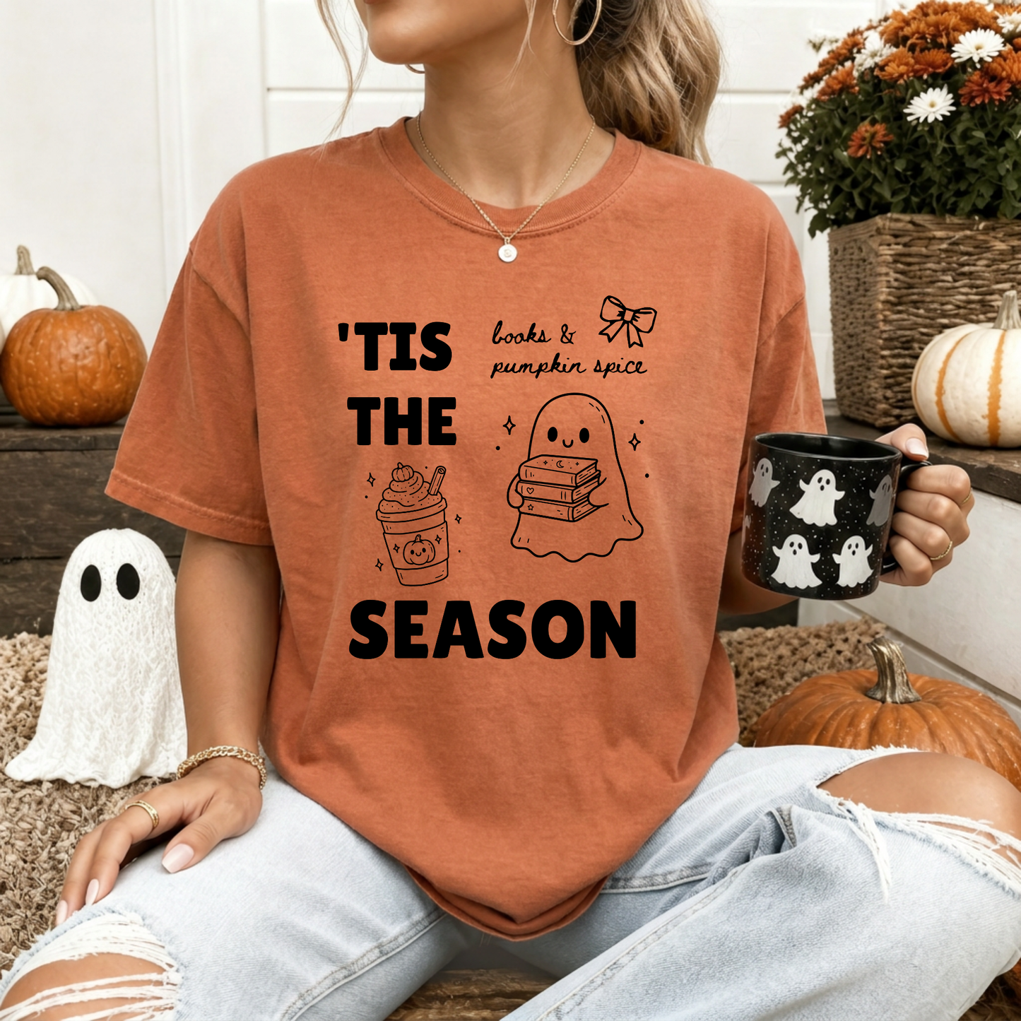 A woman wearing a Yam Orange graphic t-shirt with 'TIS THE SEASON' in bold font with cute Halloween-themed illustrations including a ghost holding a stack of books, a cute pumpkin spiced latte and a coquette bow with the phrase "books & pumpkin spice". Designed by Starlit Prose Bookish Merch Australia.