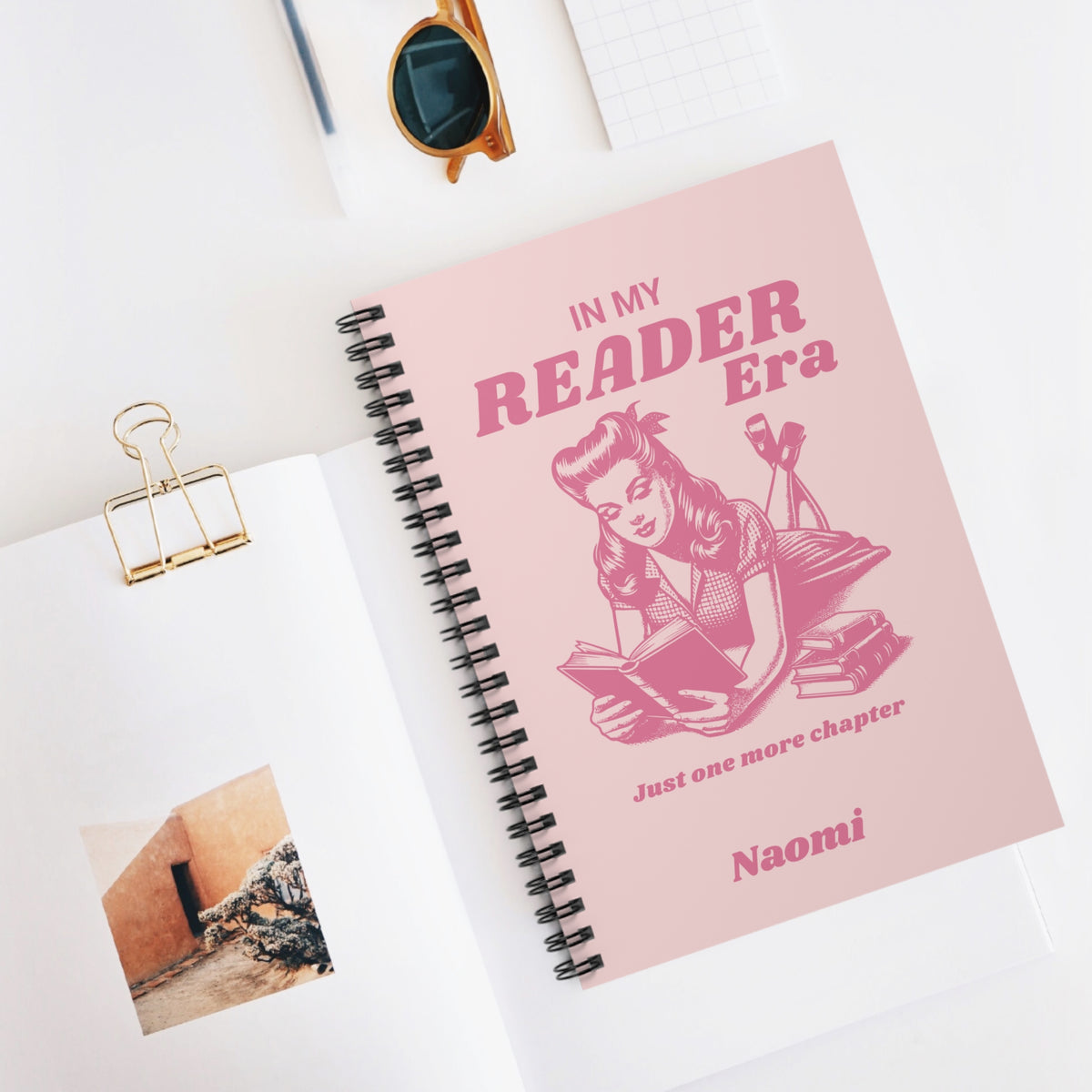 This cute bookish personalised spiral notebook features a soft light pink background, a vintage-inspired pin-up girl reading a book and the phrases "In My Reader Era" and "Just One More Chapter." A personalised section allows you to add the recipient's name, turning an already bookish design into a thoughtful gift made especially for them. Designed by Starlit Prose Bookish Merch Australia.