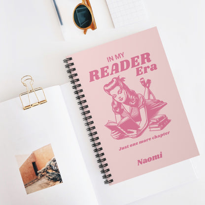 This cute bookish personalised spiral notebook features a soft light pink background, a vintage-inspired pin-up girl reading a book and the phrases "In My Reader Era" and "Just One More Chapter." A personalised section allows you to add the recipient's name, turning an already bookish design into a thoughtful gift made especially for them. Designed by Starlit Prose Bookish Merch Australia.