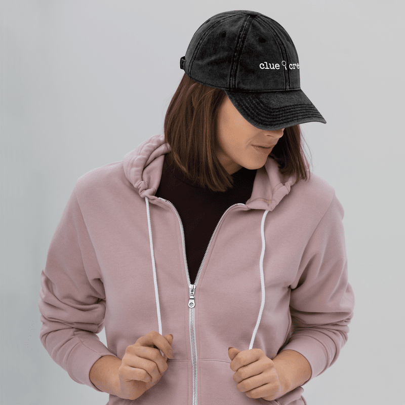A Nancy Drew vintage distressed style embroidered Dad hat features “Clue Crew” alongside a magnifying glass and tiny footsteps. Designed by Starlit Prose Bookish Merch Australia.