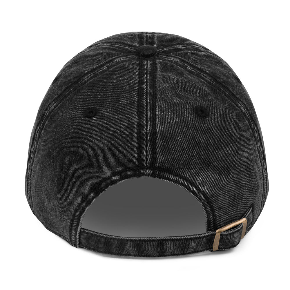 The back view of a black acid-wash baseball cap with a dark gray adjustable strap and a small gold-tone metal buckle.
