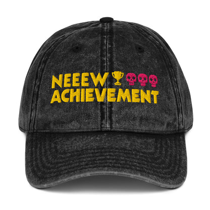 A black washed baseball cap featuring embroidered text that reads 'NEEEW ACHIEVEMENT' in yellow, with a gold trophy icon and three pink skulls.