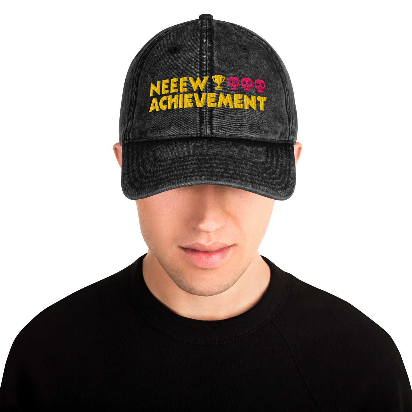 A man wearing a Dungeon Crawler Carl baseball cap with yellow and pink embroidered text reading 'NEEW ACHIEVEMENT' on a white background. Starlit Prose Bookish Merch Australia