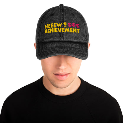 A man wearing a Dungeon Crawler Carl baseball cap with yellow and pink embroidered text reading 'NEEW ACHIEVEMENT' on a white background. Starlit Prose Bookish Merch Australia