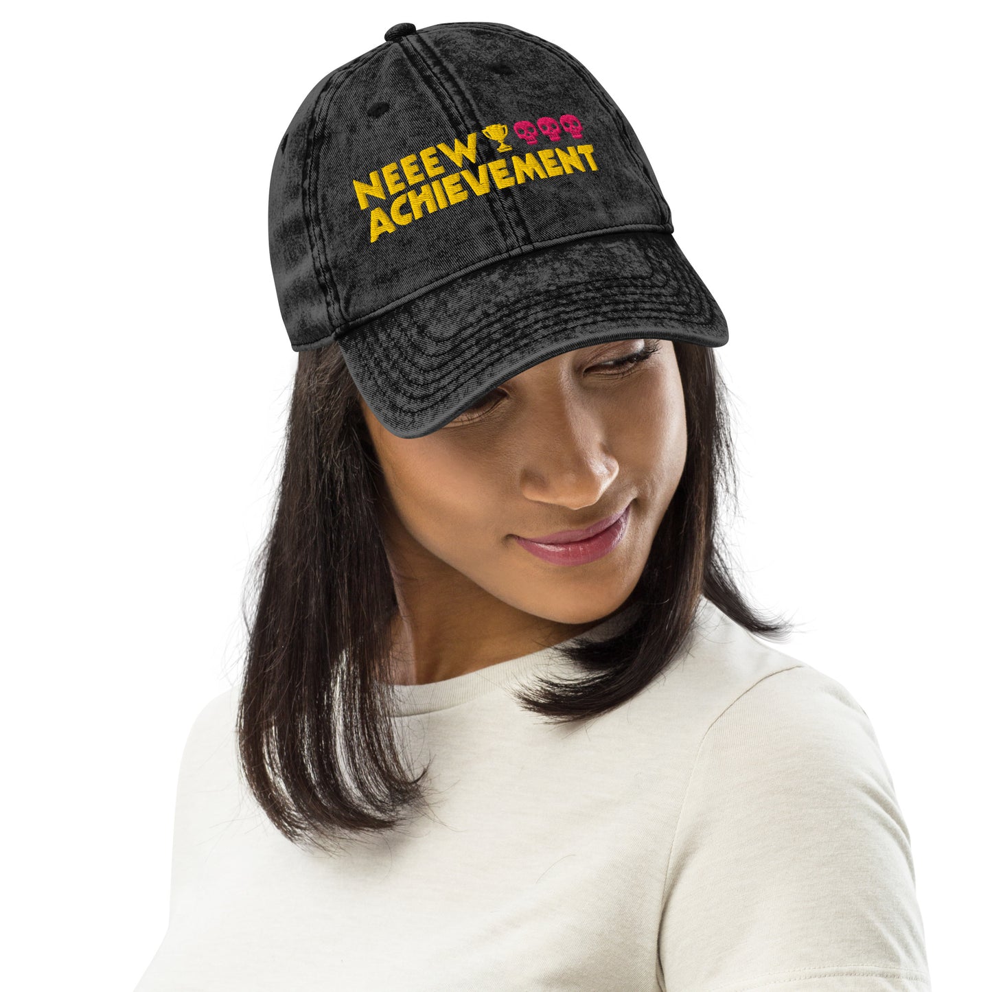 A woman wearing a black washed Dungeon Crawler Carl baseball cap with yellow and pink embroidered text reading 'NEEW ACHIEVEMENT' on a white background. Starlit Prose Bookish Merch Australia