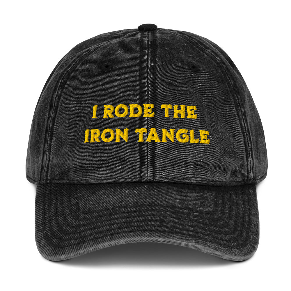 A black acid-wash baseball cap with yellow embroidered text reading 'I RODE THE IRON TANGLE' on the front, inspired by Dungeon Crawler Carl, shown against a plain white background. Starlit Prose Bookish Merch Australia