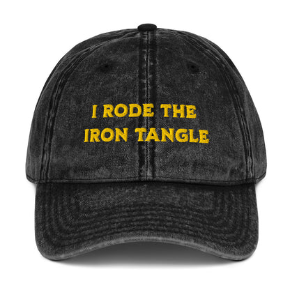 A black acid-wash baseball cap with yellow embroidered text reading 'I RODE THE IRON TANGLE' on the front, inspired by Dungeon Crawler Carl, shown against a plain white background. Starlit Prose Bookish Merch Australia