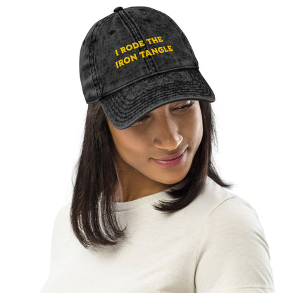 A woman wearing A black acid-wash baseball cap with yellow embroidered text reading 'I RODE THE IRON TANGLE' on the front, inspired by Dungeon Crawler Carl, shown against a plain white background. Starlit Prose Bookish Merch Australia