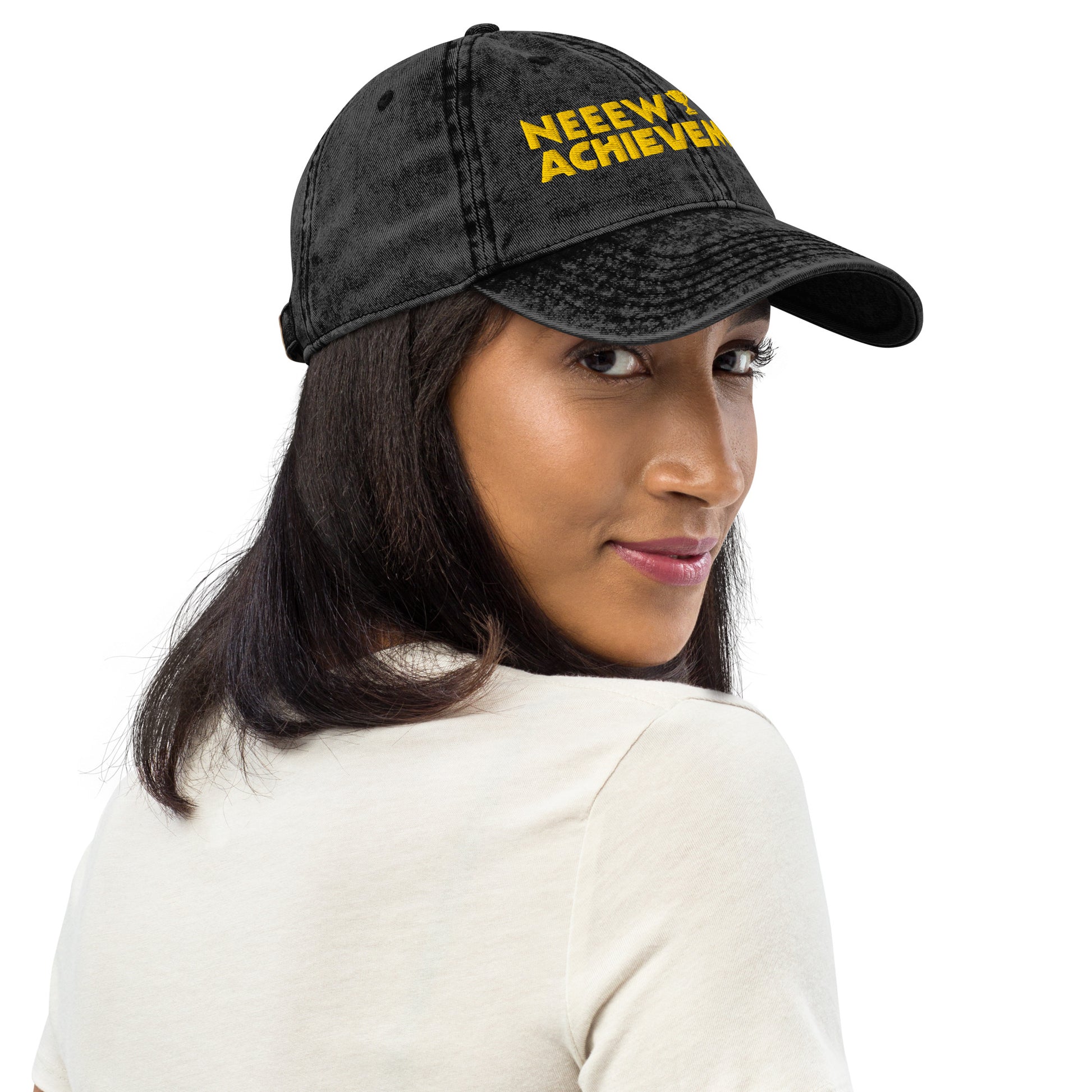 A woman wearing a black washed baseball cap Dungeon Crawler Carl baseball cap with yellow and pink embroidered text reading 'NEEW ACHIEVEMENT' on a white background. Starlit Prose Bookish Merch Australia