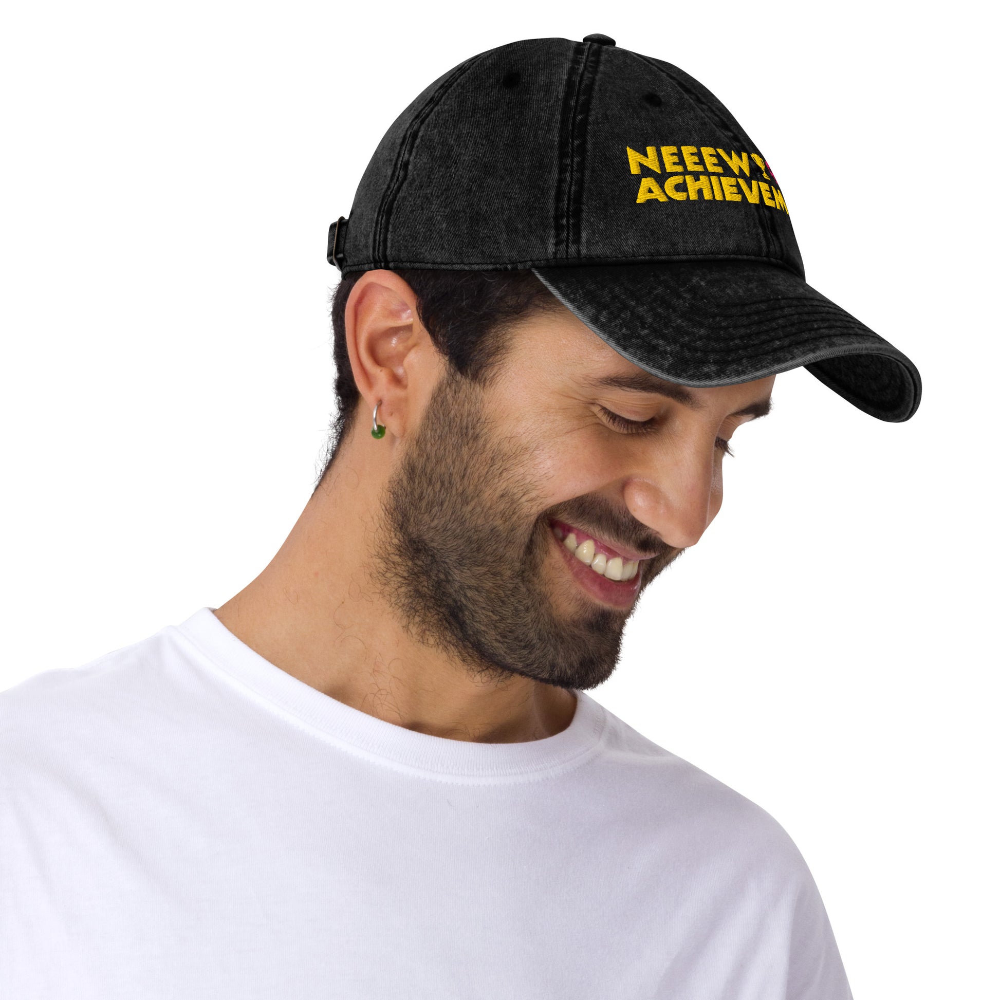 A man wearing a black washed Dungeon Crawler Carl baseball cap with yellow and pink embroidered text reading 'NEEW ACHIEVEMENT' on a white background. Starlit Prose Bookish Merch Australia paired with a white t-shirt against a plain white background.