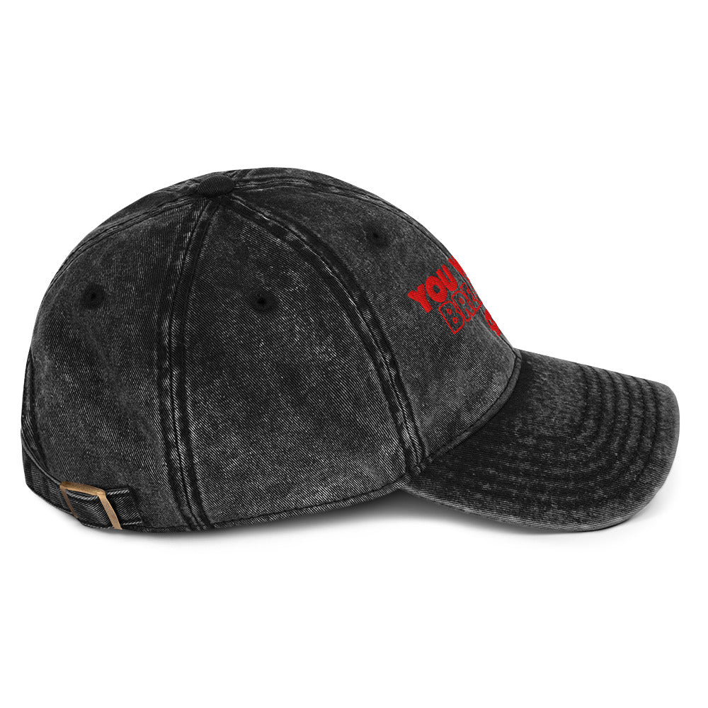 Side view of  a black acid washed denim cap, it says "You will not break me" in red embroidered text with 3 skulls. This is a quote from Dungeon Crawler Carl, it was designed by Starlit Prose Bookish Merch Australia